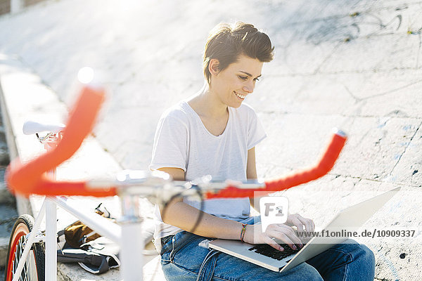 Junge Frau mit Fahrrad im Freien sitzend mit Laptop