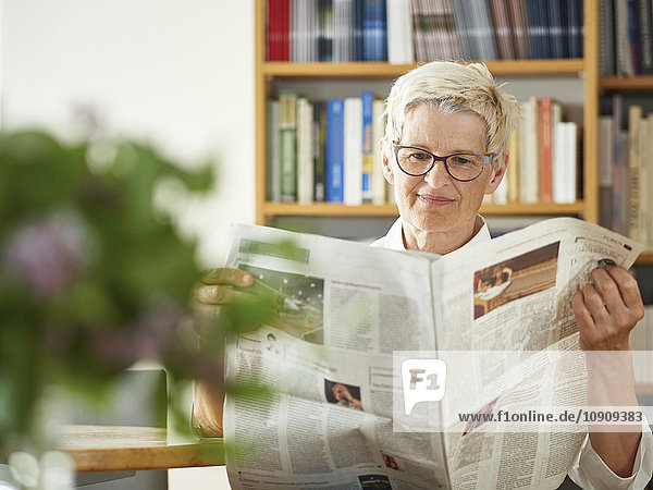 Porträt einer älteren Frau beim Zeitungslesen zu Hause