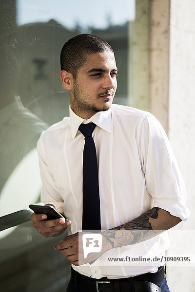 Porträt eines jungen Geschäftsmannes mit Smartphone in der Ferne