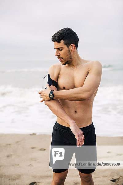 Sportive young man on the beach adjusting wearable