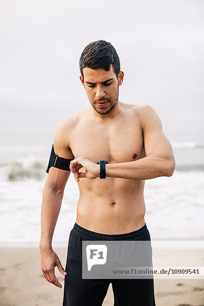 Sportive young man on the beach looking at watch