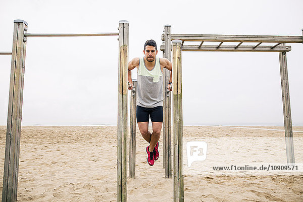 Young man exercising on bars on the beach