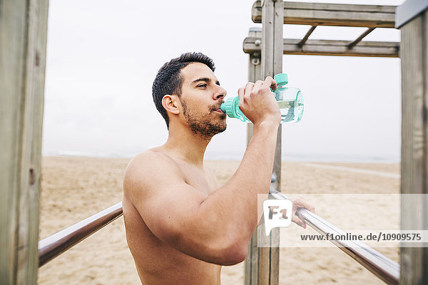 Sportler trinkt Wasser aus der Flasche am Strand