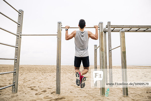 Young man doing chin-ups on the beach