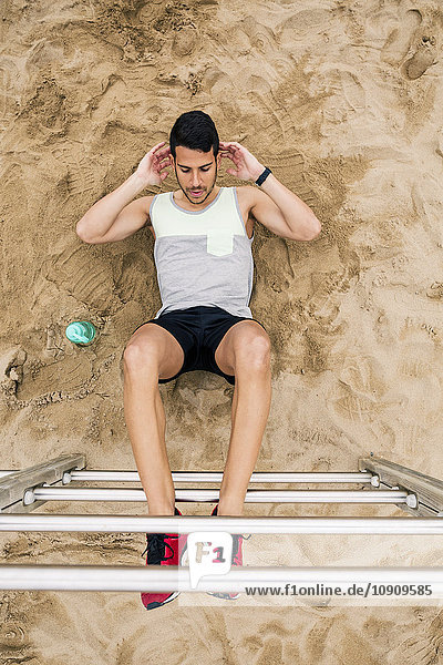 Young man doing sit-ups on wall bars on the beach