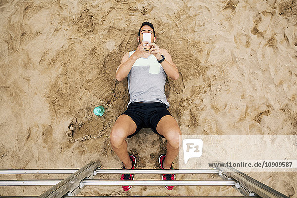 Junger Mann  der sich an den Sprossen am Strand ausruht und auf das Handy schaut