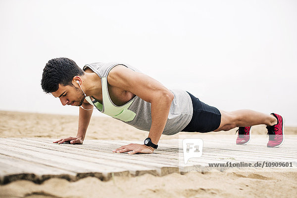 Young man doing push-ups on boardwalk on the beach