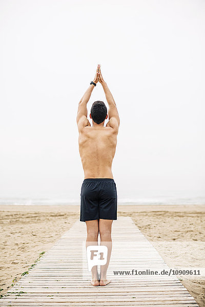 Young man practicing yoga on boardwalk on the beach