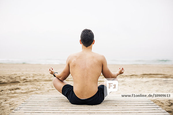 Young man practicing yoga on boardwalk on the beach