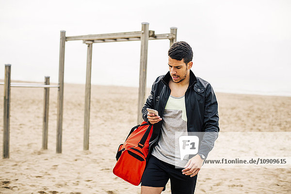 Junger Mann schaut auf Handy am Strand