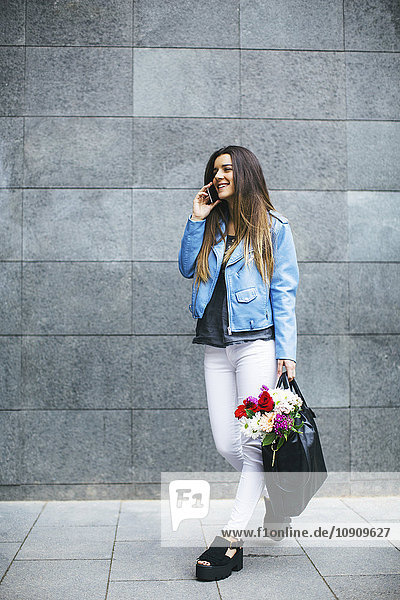 Young woman on cell phone with bunch of flowers in her bag