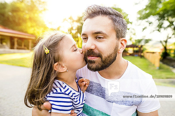 Kleines Mädchen küsst Vater auf die Wange im Park