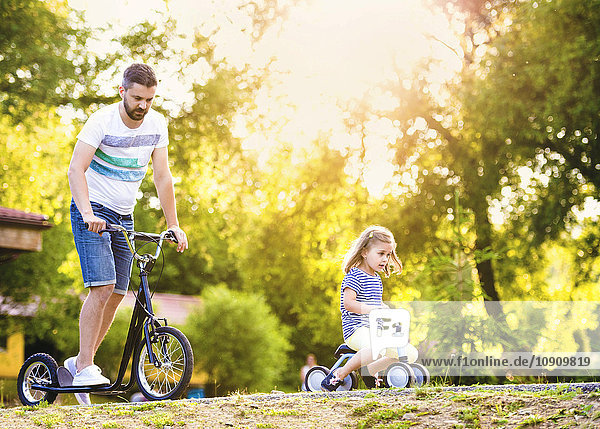 Vater und seine kleine Tochter mit Spielzeugauto und Roller im Park
