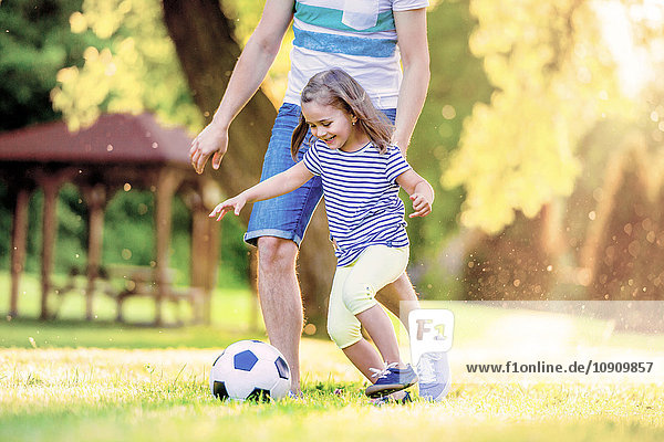 Glückliches kleines Mädchen  das mit seinem Vater im Park Fußball spielt.