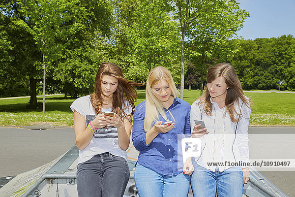 Drei Freunde sitzen Seite an Seite mit ihren Smartphones
