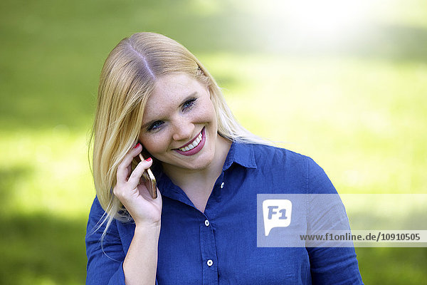 Lächelnde junge Frau telefoniert mit Smartphone im Park