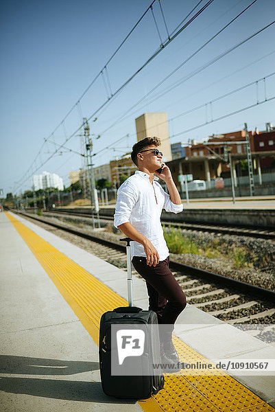 Junger Mann auf dem Handy am Bahnsteig