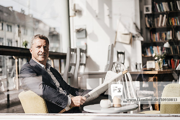 Geschäftsmann sitzt in einem Café und liest Zeitung.
