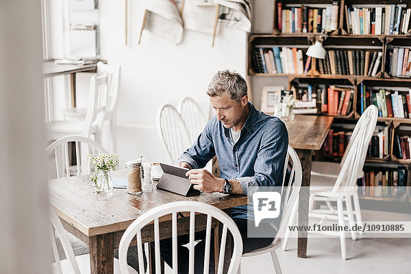 Erwachsener Mann sitzt im Cafe und liest am digitalen Tablett