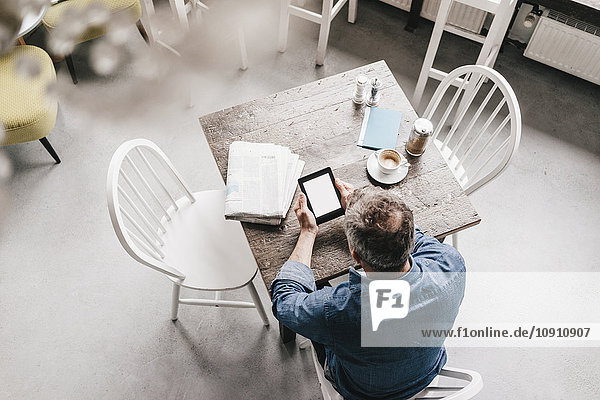 Erwachsener Mann im Café mit Zeitung und digitaler Tafel