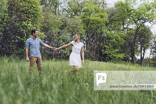 Verliebtes Paar hält sich beim Spaziergang auf einer Wiese an den Händen.