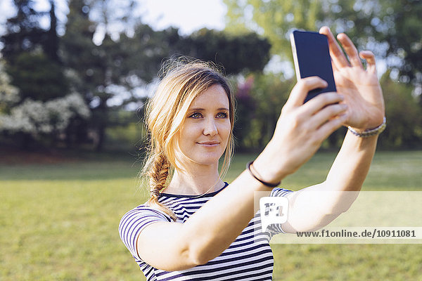 Porträt einer entspannten  blonden Frau  die sich selbst mit dem Smartphone fotografiert.