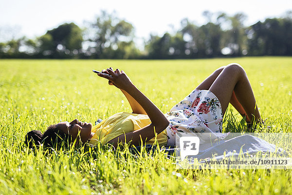 Junge Frau entspannt auf einer Wiese mit dem Smartphone