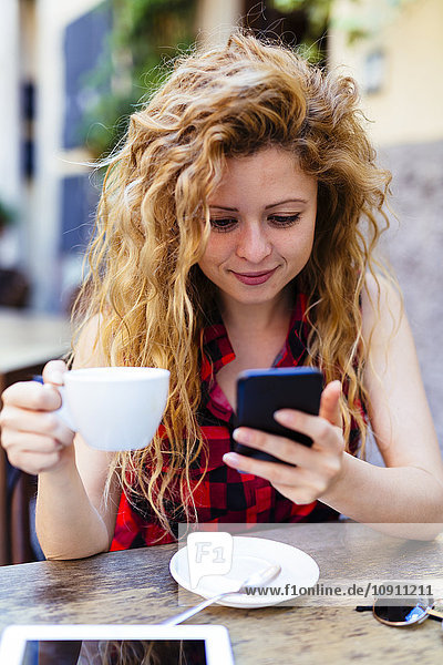 Frau im Outdoor-Café mit Blick auf das Handy