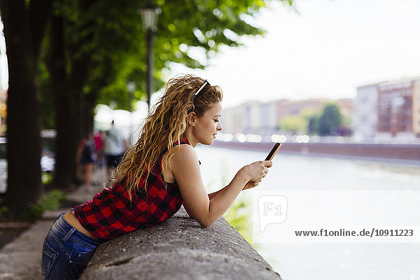 Italien  Verona  Frau am Flussufer mit Blick auf Handy