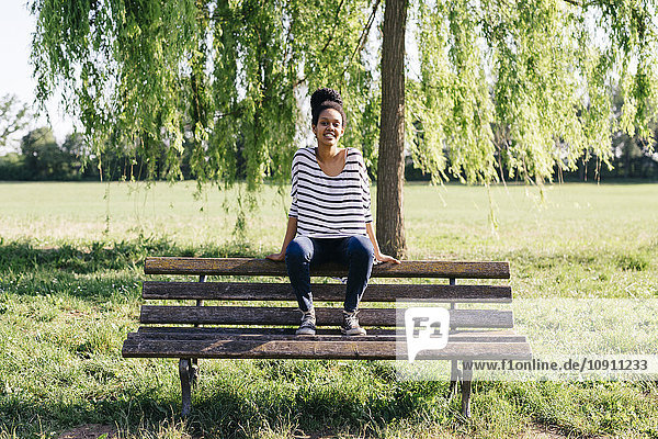 Porträt einer jungen Frau  die auf der Rückenlehne einer Parkbank sitzt.