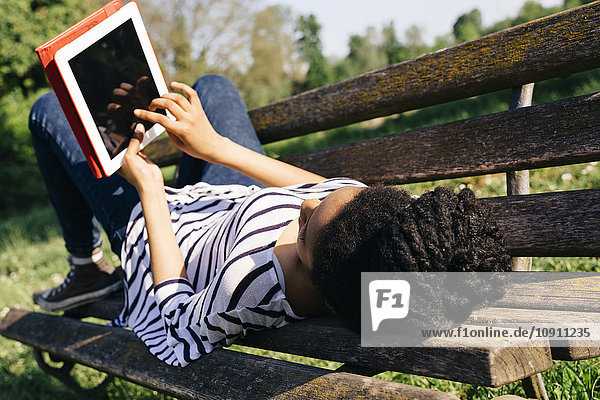 Junge Frau auf Parkbank liegend mit digitalem Tablett