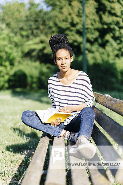 Porträt einer jungen Frau auf einer Parkbank mit Buch