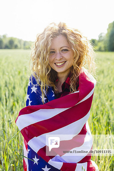 Porträt einer lächelnden Frau mit amerikanischer Flagge in der Natur