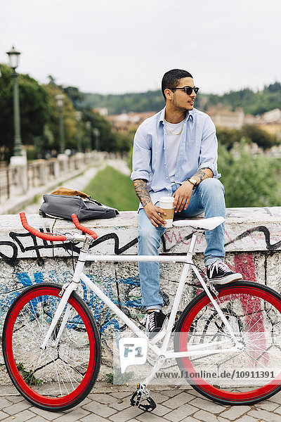 Young man with a bicycle sitting on graffiti wall