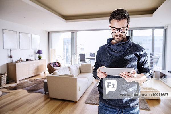 Man standing in living room  using digital tablet