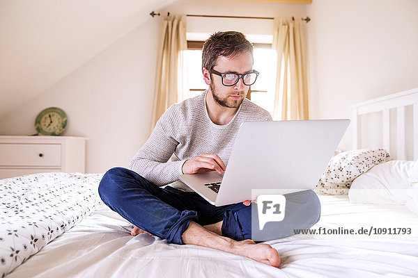 Man sitting on bed using laptop