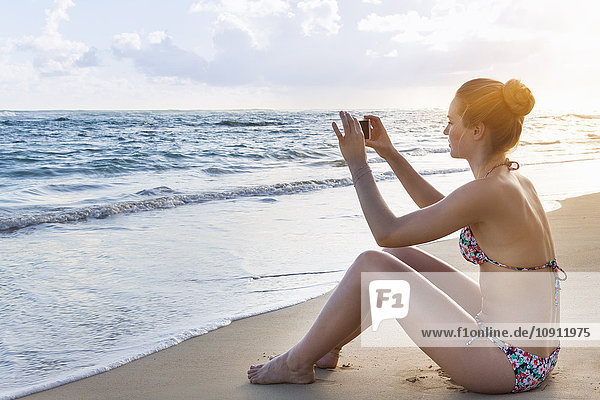 Dominican Rebublic  Young woman on tropical beach taking photo with mobile device
