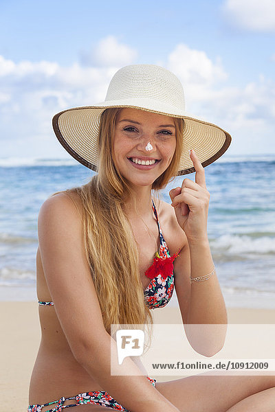 Junge Frau mit Sonnencreme am Strand