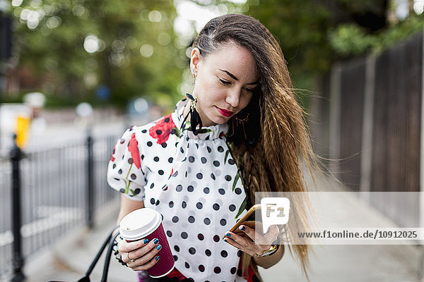 Porträt einer jungen Frau mit Kaffee zum Anschauen ihres Smartphones