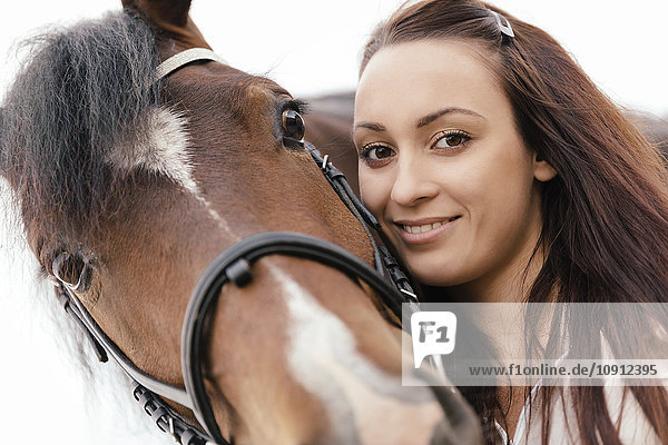Porträt einer lächelnden jungen Frau mit braunem Pferd