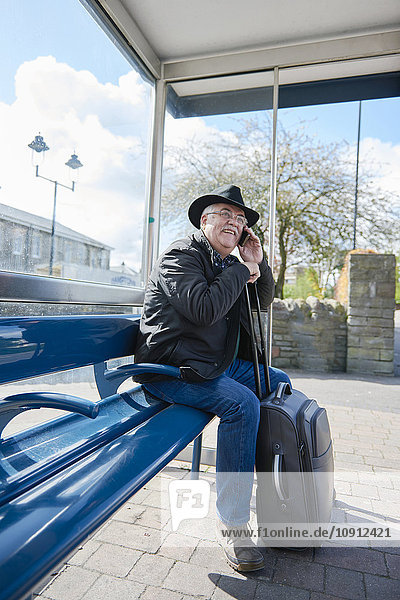 UK  Bristol  portrait of smiling senior man telephoning with smartphone while waiting at bus stop