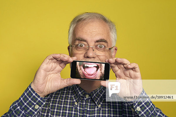 Porträt eines älteren Mannes  der ein Smartphone in der Hand hält  mit Fotografie des geöffneten Mundes.