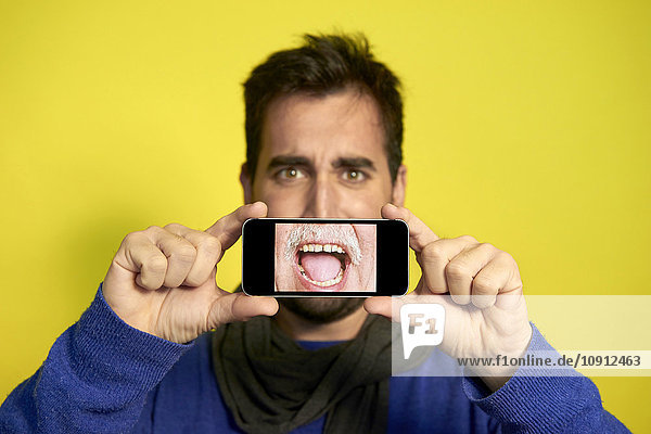 Porträt eines Mannes  der ein Smartphone hält  mit Fotografie des schreienden Mundes eines anderen Mannes.