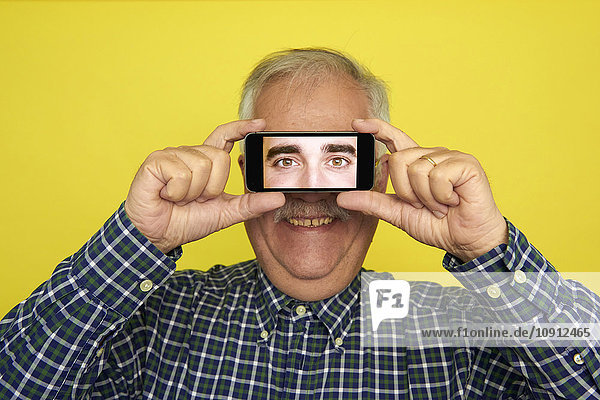 Porträt eines lächelnden älteren Mannes  der ein Smartphone hält und die Augen eines anderen Mannes fotografiert.