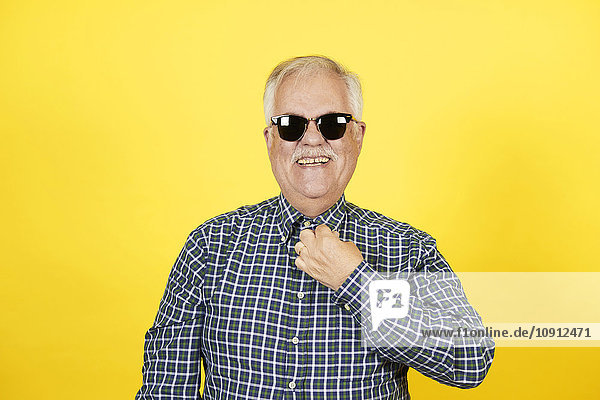 Porträt eines lächelnden älteren Mannes mit Sonnenbrille vor gelbem Hintergrund