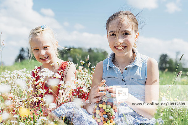 Two happy girls in meadow with glass with jelly beans