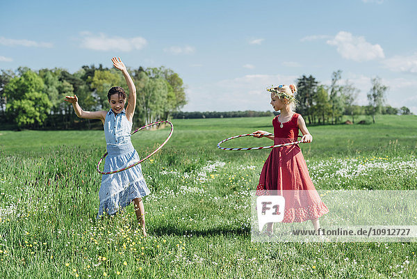 Two girls with hula hoops in meadow
