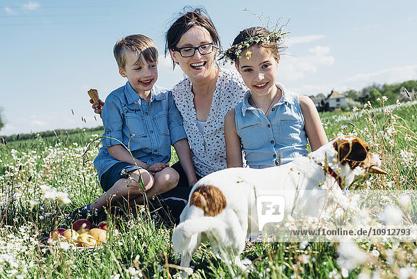 Glückliche Mutter und zwei Kinder mit Hund auf der Wiese