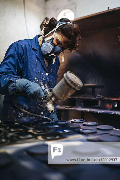 Arbeiterinnen bemalen Keramik mit Spritzpistole
