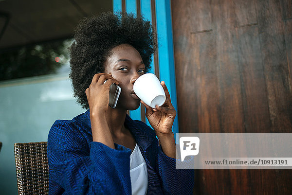 Portrait of young woman talking on mobile phone while drinking coffee in a street cafe